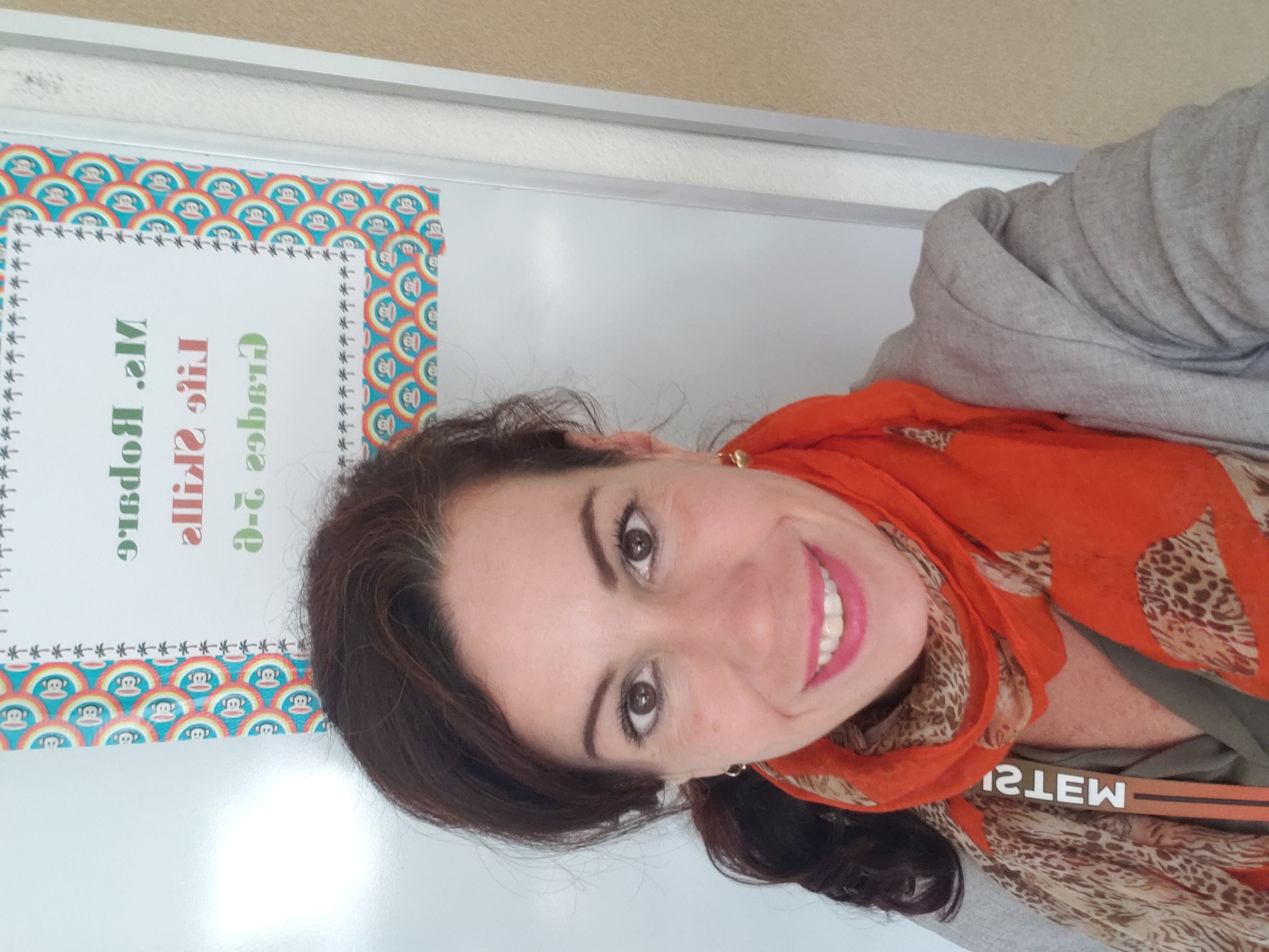 A picture of Ms. Danielle Robare standing in front of her whiteboard wearing the Austin school colors. 